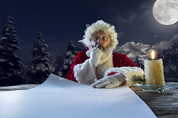 Image showing Emotional Santa Claus congratulating with New Year and Christmas, writing a letter, wish list in midnight with candle