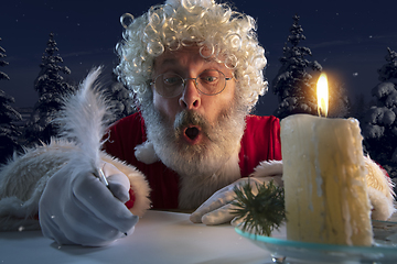 Image showing Emotional Santa Claus congratulating with New Year and Christmas, writing a letter, wish list in midnight with candle