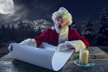 Image showing Emotional Santa Claus congratulating with New Year and Christmas, writing a letter, wish list in midnight with candle