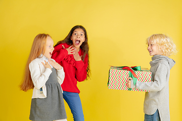 Image showing Giving and getting presents on Christmas holidays. Group of happy smiling children having fun isolated on yellow studio background