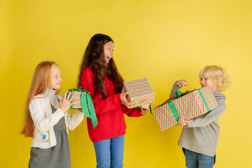 Image showing Giving and getting presents on Christmas holidays. Group of happy smiling children having fun isolated on yellow studio background