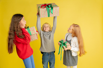 Image showing Giving and getting presents on Christmas holidays. Group of happy smiling children having fun isolated on yellow studio background