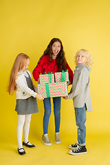 Image showing Giving and getting presents on Christmas holidays. Group of happy smiling children having fun isolated on yellow studio background