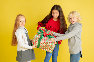 Image showing Giving and getting presents on Christmas holidays. Group of happy smiling children having fun isolated on yellow studio background