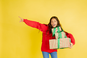 Image showing Giving and getting presents on Christmas holidays. Teen girl having fun isolated on yellow studio background