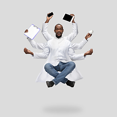 Image showing Handsome multi-armed doctor levitating isolated on grey studio background with equipment