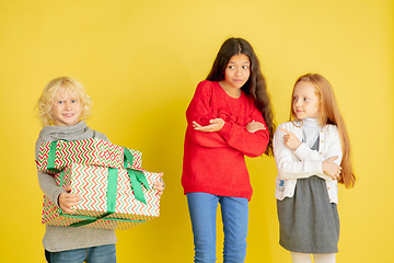 Image showing Giving and getting presents on Christmas holidays. Group of happy smiling children having fun isolated on yellow studio background