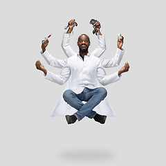 Image showing Handsome multi-armed doctor levitating isolated on grey studio background with equipment