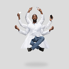 Image showing Handsome multi-armed doctor levitating isolated on grey studio background with equipment