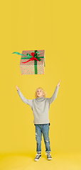 Image showing Giving and getting presents on Christmas holidays. Little boy having fun isolated on yellow studio background