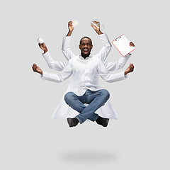 Image showing Handsome multi-armed doctor levitating isolated on grey studio background with equipment