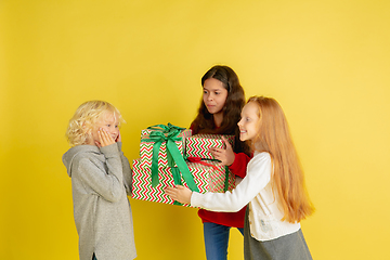 Image showing Giving and getting presents on Christmas holidays. Group of happy smiling children having fun isolated on yellow studio background