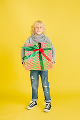 Image showing Giving and getting presents on Christmas holidays. Little boy having fun isolated on yellow studio background