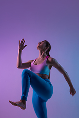 Image showing Young sportive woman training isolated on gradient studio background in neon light. athletic and graceful