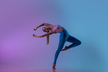 Image showing Young sportive woman training isolated on gradient studio background in neon light. athletic and graceful