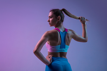 Image showing Young sportive woman training isolated on gradient studio background in neon light. athletic and graceful