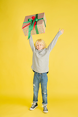 Image showing Giving and getting presents on Christmas holidays. Little boy having fun isolated on yellow studio background