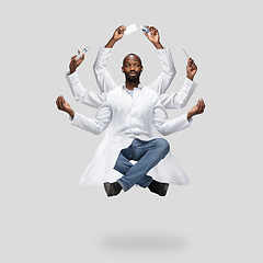 Image showing Handsome multi-armed doctor levitating isolated on grey studio background with equipment