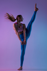 Image showing Young sportive woman training isolated on gradient studio background in neon light. athletic and graceful