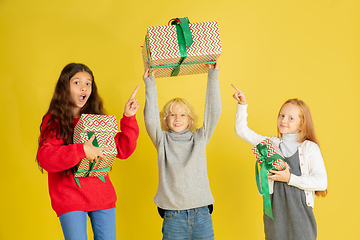 Image showing Giving and getting presents on Christmas holidays. Group of happy smiling children having fun isolated on yellow studio background