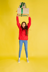 Image showing Giving and getting presents on Christmas holidays. Teen girl having fun isolated on yellow studio background