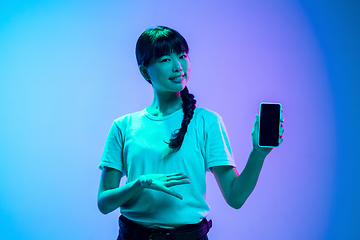 Image showing Young asian woman\'s portrait on gradient blue-purple studio background in neon light