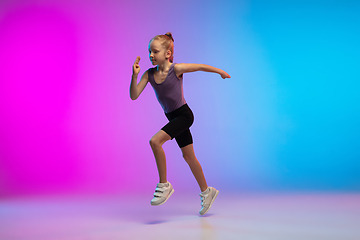 Image showing Teenage girl running, jogging against gradient pink-blue neon studio background in motion