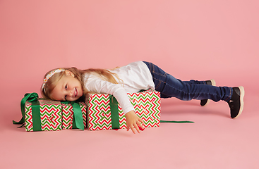 Image showing Giving and getting presents on Christmas holidays. Little smiling girl having fun isolated on pink studio background