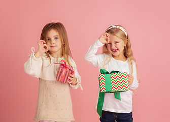 Image showing Giving and getting presents on Christmas holidays. Two little smiling children having fun isolated on pink studio background