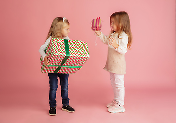 Image showing Giving and getting presents on Christmas holidays. Two little smiling children having fun isolated on pink studio background