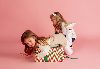 Image showing Giving and getting presents on Christmas holidays. Two little smiling children having fun isolated on pink studio background