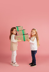 Image showing Giving and getting presents on Christmas holidays. Two little smiling children having fun isolated on pink studio background