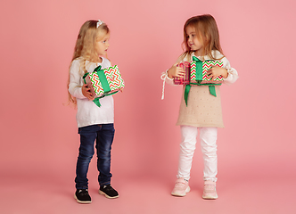 Image showing Giving and getting presents on Christmas holidays. Two little smiling children having fun isolated on pink studio background