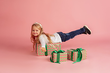 Image showing Giving and getting presents on Christmas holidays. Little smiling girl having fun isolated on pink studio background