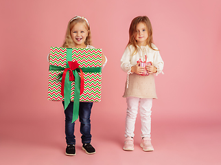 Image showing Giving and getting presents on Christmas holidays. Two little smiling children having fun isolated on pink studio background