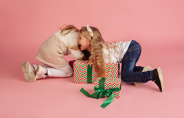 Image showing Giving and getting presents on Christmas holidays. Two little smiling children having fun isolated on pink studio background