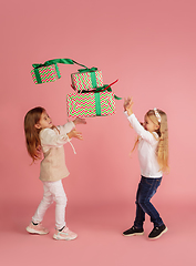 Image showing Giving and getting presents on Christmas holidays. Two little smiling children having fun isolated on pink studio background