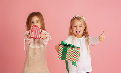 Image showing Giving and getting presents on Christmas holidays. Two little smiling children having fun isolated on pink studio background