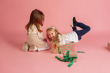 Image showing Giving and getting presents on Christmas holidays. Two little smiling children having fun isolated on pink studio background