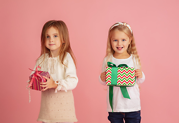 Image showing Giving and getting presents on Christmas holidays. Two little smiling children having fun isolated on pink studio background