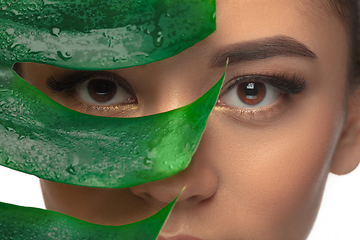 Image showing Close up young woman\'s portrait with monstera leaf on white background. Cosmetics and makeup, natural and eco treatment, skin care.