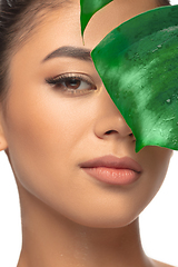 Image showing Close up young woman\'s portrait with monstera leaf on white background. Cosmetics and makeup, natural and eco treatment, skin care.