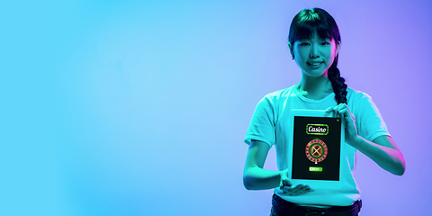 Image showing Online gambling, casino concept. Young asian woman holding devices with lottery, casino cover in neon light