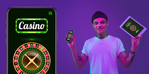 Image showing Online gambling, casino concept. Young man holding devices with lottery, casino cover in neon light