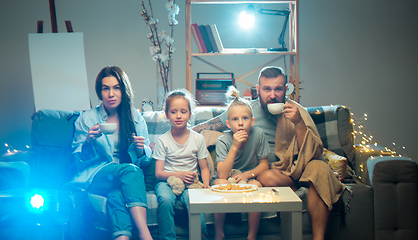 Image showing Happy family watching projector, TV, movies with popcorn in the evening at home. Mother, father and kids spending time together.