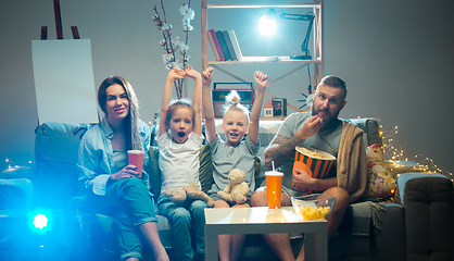 Image showing Happy family watching projector, TV, movies with popcorn in the evening at home. Mother, father and kids spending time together.