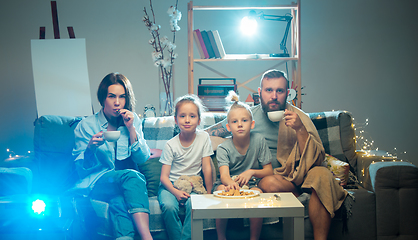 Image showing Happy family watching projector, TV, movies with popcorn in the evening at home. Mother, father and kids spending time together.