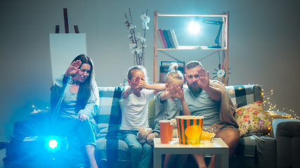 Image showing Happy family watching projector, TV, movies with popcorn in the evening at home. Mother, father and kids spending time together.