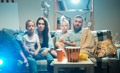 Image showing Happy family watching projector, TV, movies with popcorn in the evening at home. Mother, father and kids spending time together.