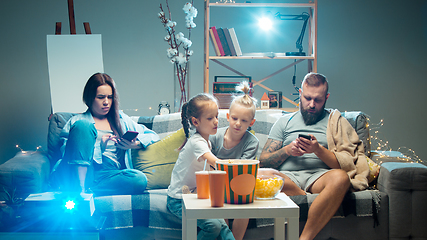 Image showing Happy family watching projector, TV, movies with popcorn in the evening at home. Mother, father and kids spending time together.